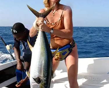 woman on a fishing boat in Zanzibar with a local expert fisherman, lifting a large kingfish during a fishing tour experience