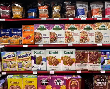 Cereal aisle at Round Hill Market featuring brands like KIND, Cascadian Farm, Kashi, Cheerios, and Lucky Charms.