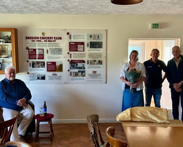 A group of people standing around a wall mounted timeline showing a history of Bredon Cricket Club