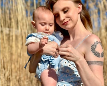 A mother and baby girl both wearing matching blue dresses in a hay field on a sunny day, symboling maternal love.