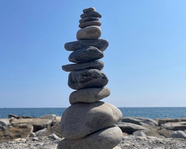 des galets empilés pour former un cairn avec en fond la mer et le ciel bleu