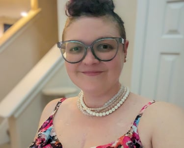 Picture of Megan, a smiling woman with a blue mohawk and pearls.