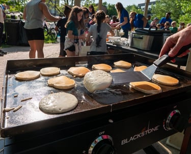 A hand flipping pancakes with a spatula, with people in the background