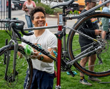 A young man smiling and washing a bike held high on a stand