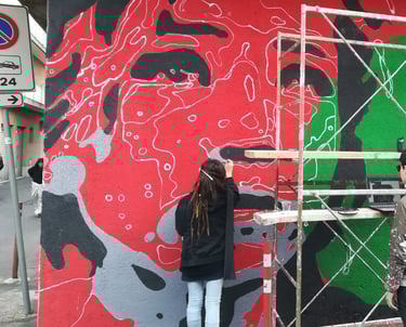 Red and green mural in progress, Poliops and collaborators painting on urban scaffolding.