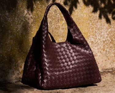Bottega Veneta Luxury woven leather handbag in deep brown displayed outdoors.