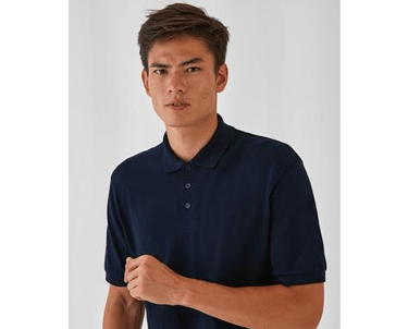 a man in a blue shirt and jeans standing in front of a white wall