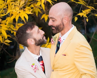 Pareja de hombres gay casados con ropa colorida, mirándose enamorados. Bodas LGBTQ+ en España."
