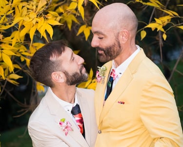 Pareja de hombres gay casados con ropa colorida, mirándose enamorados. Bodas LGBTQ+ en España."