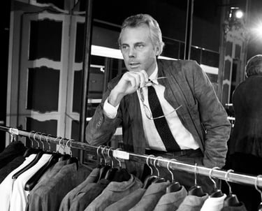 Young Giorgio Armani in his fashion studio with clothing rack.
