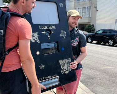 two men carrying a prototype photobooth made from wood