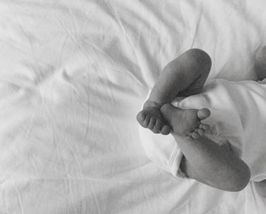 bas du corps d'un bebe allonger sur un lit avec des draps blancs