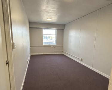 Small unfurnished office with dark carpet and 1 window on the far wall