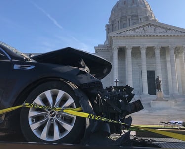 The front of a car that has been in a wreck, with the Missouri capital building in the background