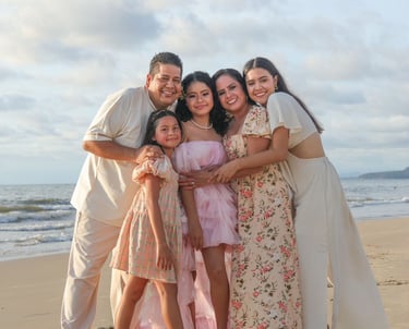 una familia de mamá, 3 hijas y papá sonriendo a la cámara en la playa