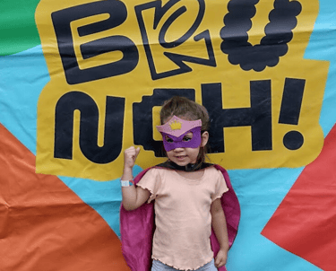 a little girl in a pink capelet and a pink capelet, behind text "brunch" in the petit brunch event