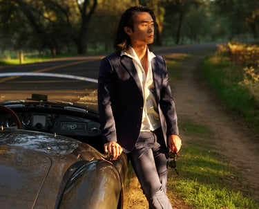 A man leaning against the passenger side of a 1958 MG MGA Roadster in a park during golden hour.
