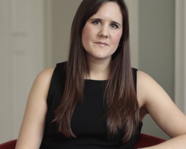 Photo of Anna Joyce, CBTI insomnia therapist in UK, sitting in red chair wearing a black dress