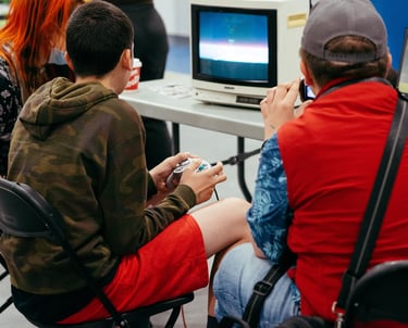 Close up image of two people sitting at an old tv playing some video games together at the event.