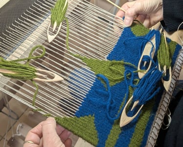 Stagiaire tissant un kilim géométrique en bleu et vert sur un métier à tisser avec navettes