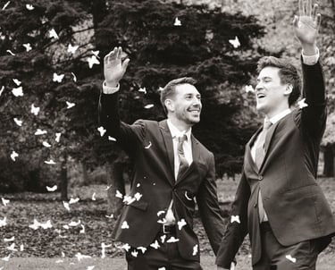 Pareja de recién casados gays sonriendo y lanzando pétalos de rosa mientras se toman de la mano. Gay wedding celebration.