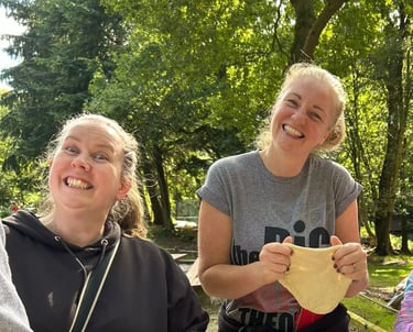Two leaders smile at the camera while stretching dough for the 25th Allerton scout camp