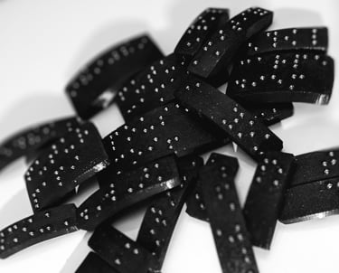 Plaque en braille, empilée de manière aléatoire, avec des points en relief bien visible