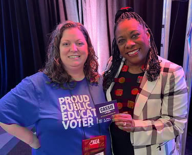 Woman in blue shirt standing with a black woman holding a campaign sticker
