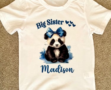 White childs t-shirt with a Panda Bear wearing a blue bow, reading "Big Sister" & personalized with childs name.