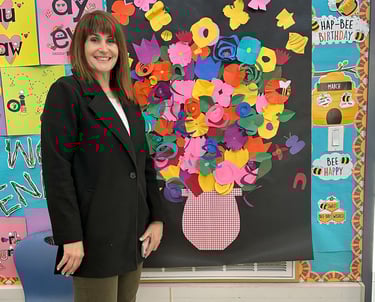 a teacher standing by a collage of paper flowers