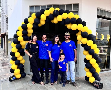 4 adultos e 1 criança com uniformes azuis, em frente a loja de baterias automotivas