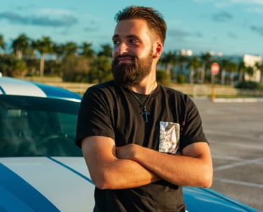 white man with a beard looking to the side sitting on a blue car hood