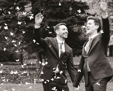 Pareja de recién casados gays sonriendo y lanzando pétalos de rosa mientras se toman de la mano. Gay wedding celebration.