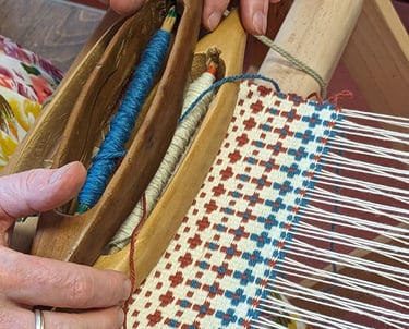 Wooden shuttles and thread spools are used to weave blue, brown, and white crosses on a weaving loom