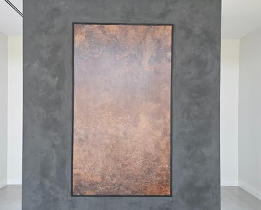 Bold black limewash wall with a rectangular copper wallpaper inset, combining textured depth with warm metallic contrast