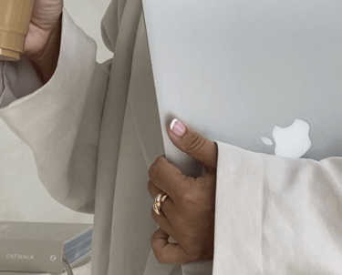 Ženska osoba, poslovna, u ruci drži Macbook, u drugoj ledenu kavu.
