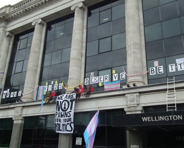 Activists sitting on top of NHS England offices with a banner "we are not prawns for your politics"