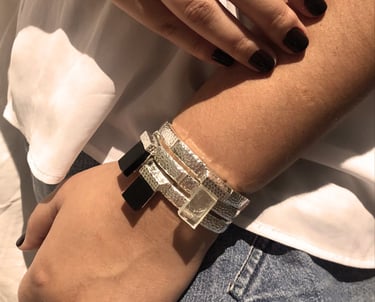 as mãos de uma mulher com um mix de pulseiras pratas com cristais e obsidiana negra