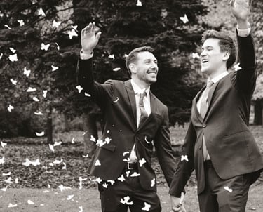 Pareja de recién casados gays sonriendo y lanzando pétalos de rosa mientras se toman de la mano. Gay wedding celebration.