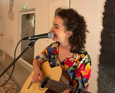 Une femme musicienne qui joue de la guitare et qui chante dans un micro sur pied