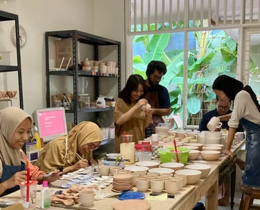 a group of people laughing together while sitting at a table making handmade pottery