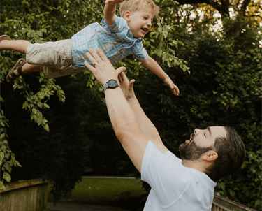 Brian Hess, owner, throwing son up in the air with trees in the background