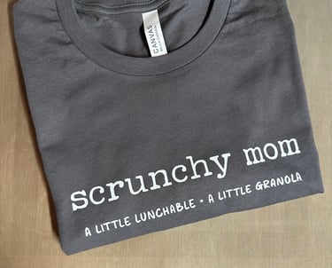 Gray folded t-shirt showing the white text that reads, "scrunchy mom - a little lunchable a little granola."