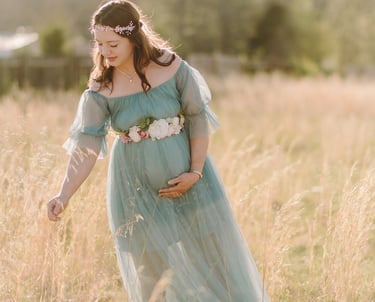 a pregnant woman in a blue dress standing in a field