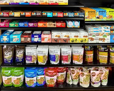 Round Hill Market snack aisle with various brands including Purely Elizabeth, Kind, Think!, and Pretzel Crisps.