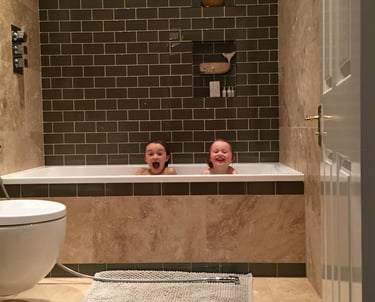 Two children pulling cheeky faces in the bath. 