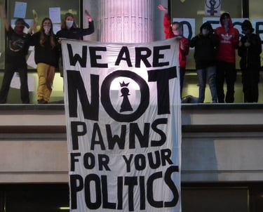 Activists standing on top of NHS England offices with a banner "we are not prawns for your politics"