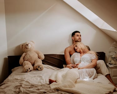 une femme enceinte pose dans son lit avec son conjoint pour une séance photo grossesse