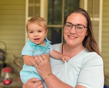 a woman in glasses and a blue shirt holding a baby