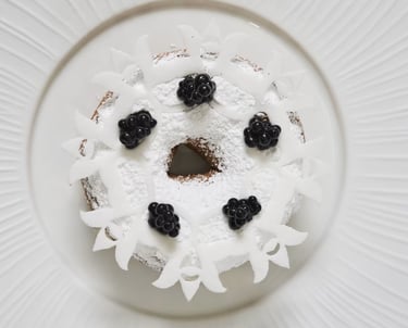 Powdered sugar dessert topped with blackberries and white chocolate curls.
